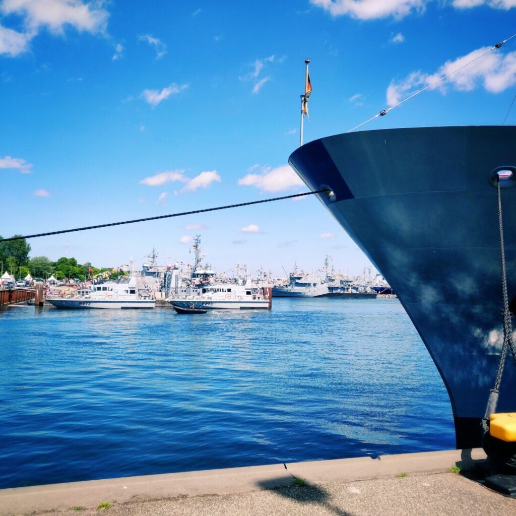 Ein Blick auf den Hafen mit mehreren Schiffen im Wasser, einem klaren blauen Himmel und einer großen Schiffsspitze im Vordergrund, die an einem Tau befestigt ist.