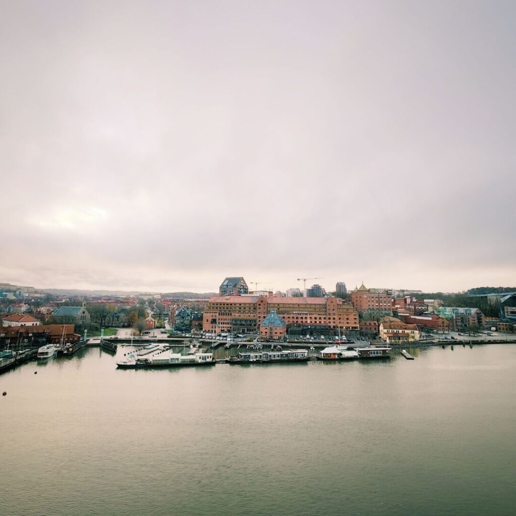 Die Aussicht zeigt eine ruhige Hafenlandschaft mit historischen und modernen Gebäuden entlang des Wassers, unter einem bewölkten Himmel, der die sanften Farben des Tages widerspiegelt.
