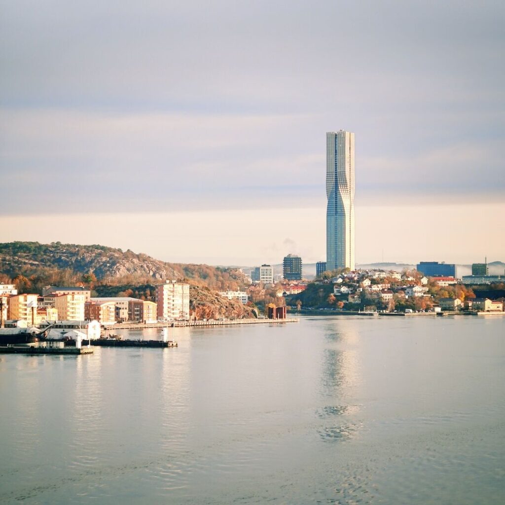 Moderne Architektur und Natur vereinen sich in einer Stadtansicht mit einem hohen Turm und ruhigem Wasser.