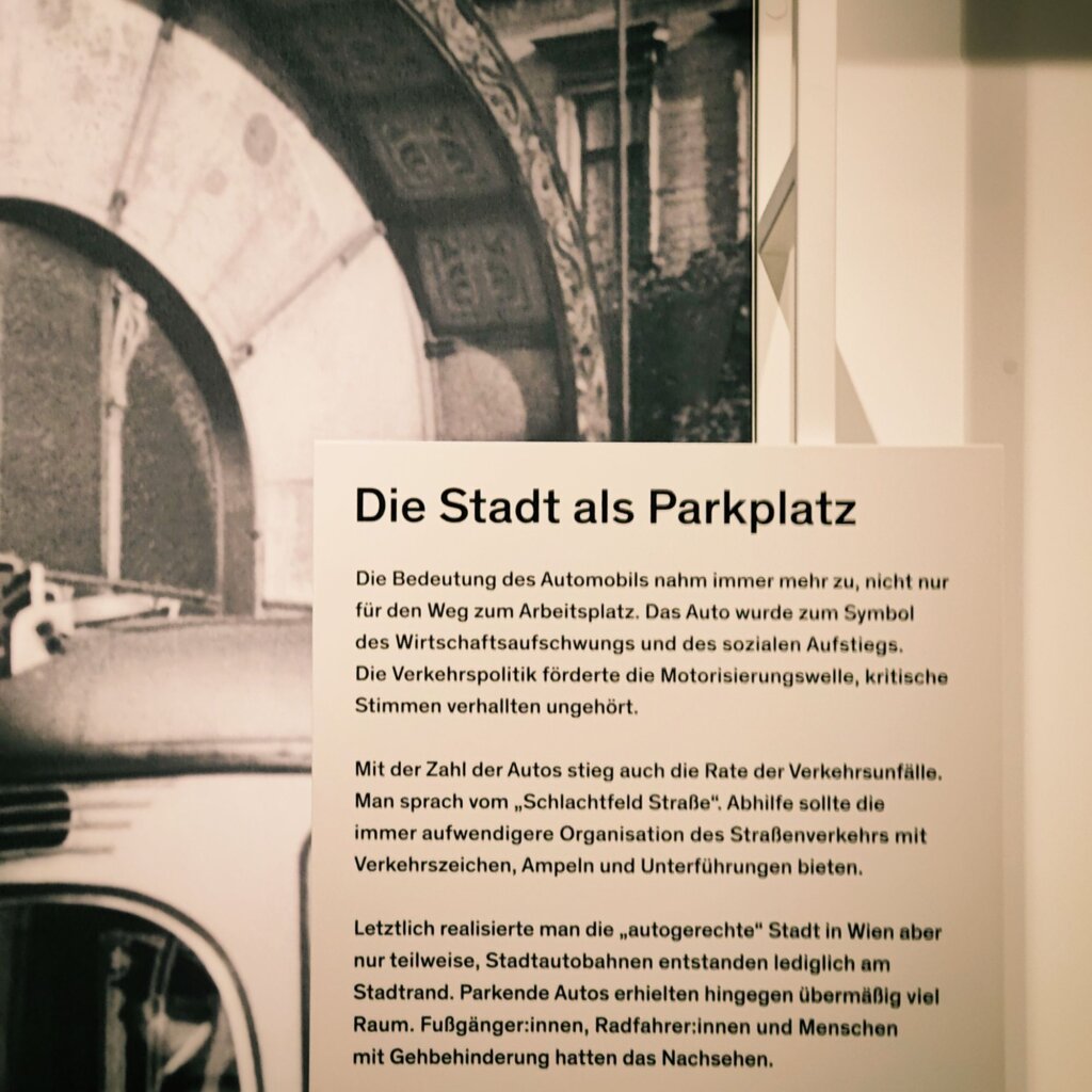 Eine informative Ausstellungstafel thematisiert die wachsende Bedeutung des Automobils in der Stadt, die Herausforderungen durch Verkehrsunfälle und die Entwicklung städtischer Infrastruktur für Fußgänger und Radfahrer.